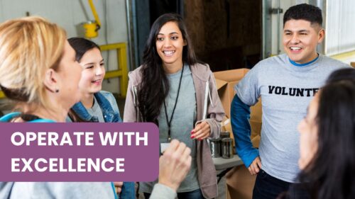 A professional but casual meeting between four people—two men and two women—at a long wooden table. The woman in the center is smiling and engaged in conversation with the man across from her, illustrating effective communication and collaboration within a nonprofit organization team.
